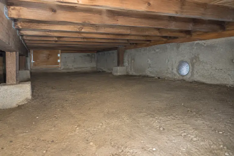 Crawl space cleanup under a raised floor, after: Clean crawl space with a screened foundation vent.