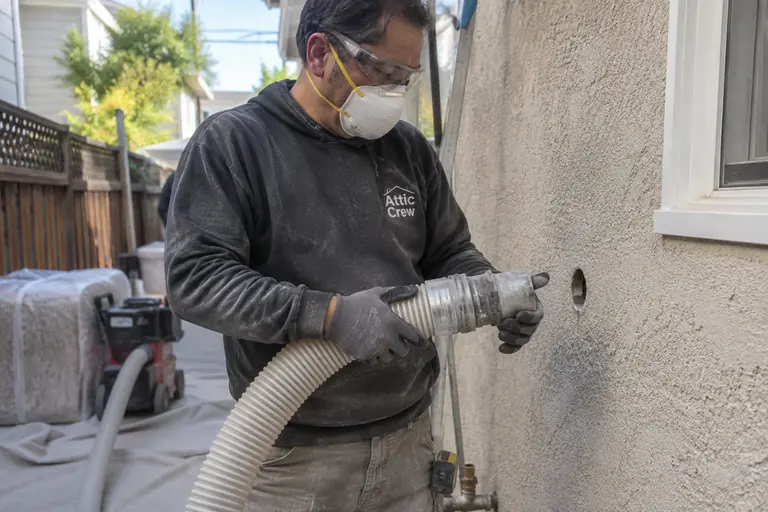 Blowing insulation into an exterior stucco wall through a drilled port.