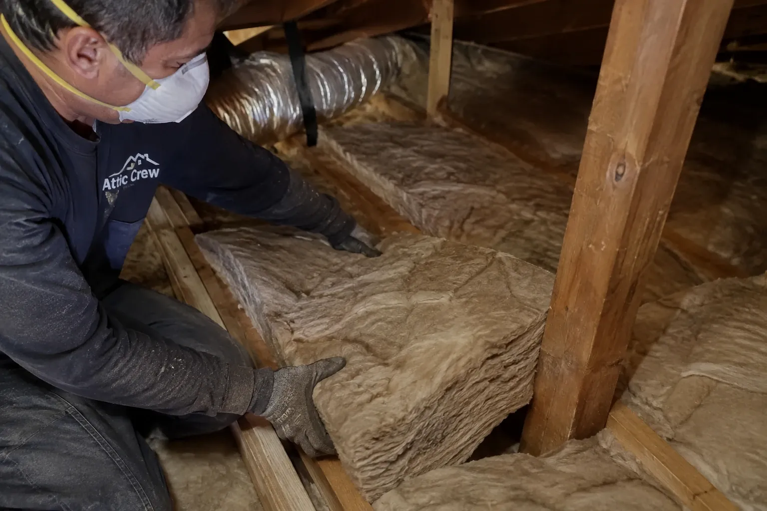 Fitting new batt insulation between the attic joists.